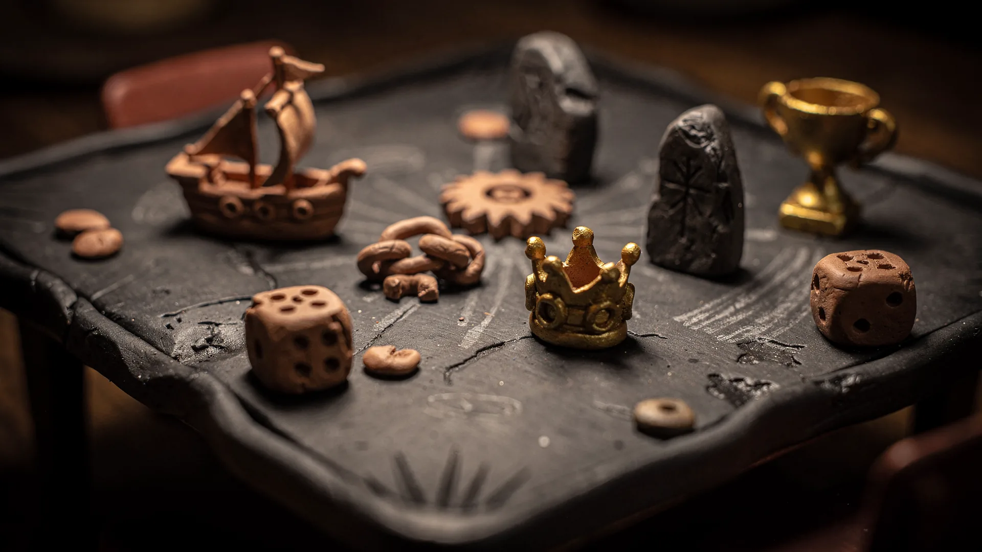 A games table built of dark clay scattered with small handmade playing pieces shaped as tiny history artefacts, clay dice mid-tumble, one small gold trophy